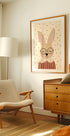 útulná obývačka s béžovým kreslom, drevenou komodou a zarámovaným obrazom králika v okuliaroch.