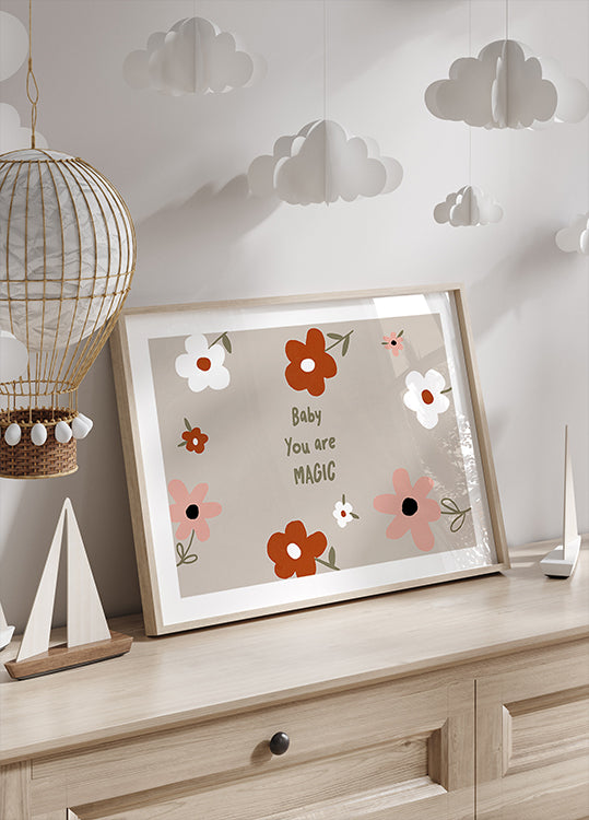 Op engem hëlzenen Kommoud steet e kadréiertem Drock mat engem Blummendesign an den Text "Baby You are Magic" mat enger dekorativer Pabeierslantern driwwer hänken.